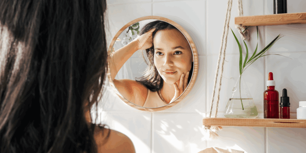Mulher analisando seu tipo de pele no espelho para montar uma rotina de skincare.