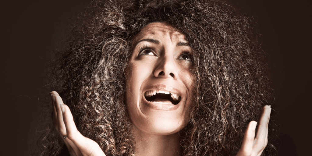 Mulher com cabelo cacheado olhando frustrada para o frizz em seu cabelo.