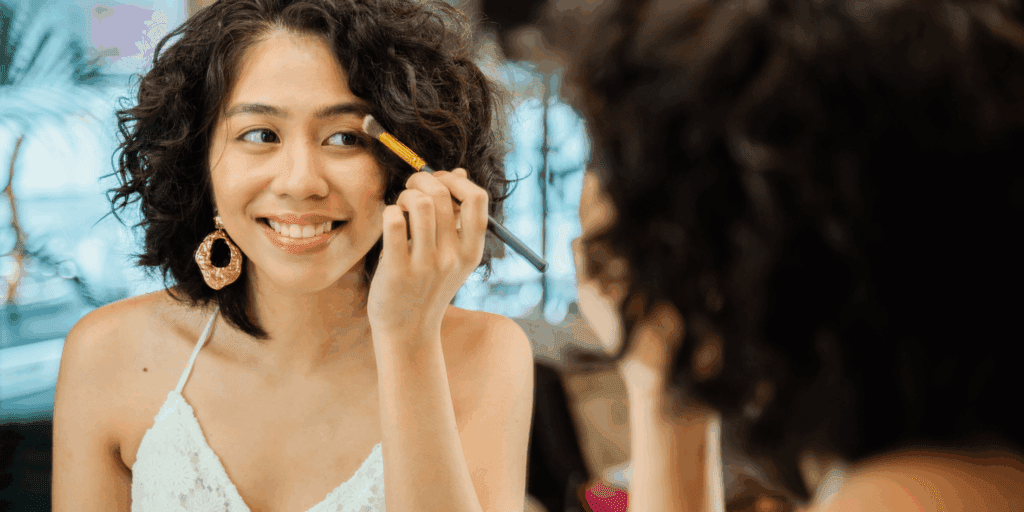 Mulher jovem com maquiagem natural, sorrindo e segurando pincéis, ideal para iniciantes em maquiagem.