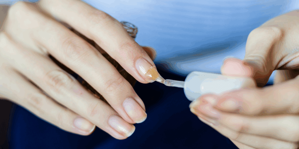 mãos de mulher aplicando base fortalecedora em unhas curtas e em recuperação