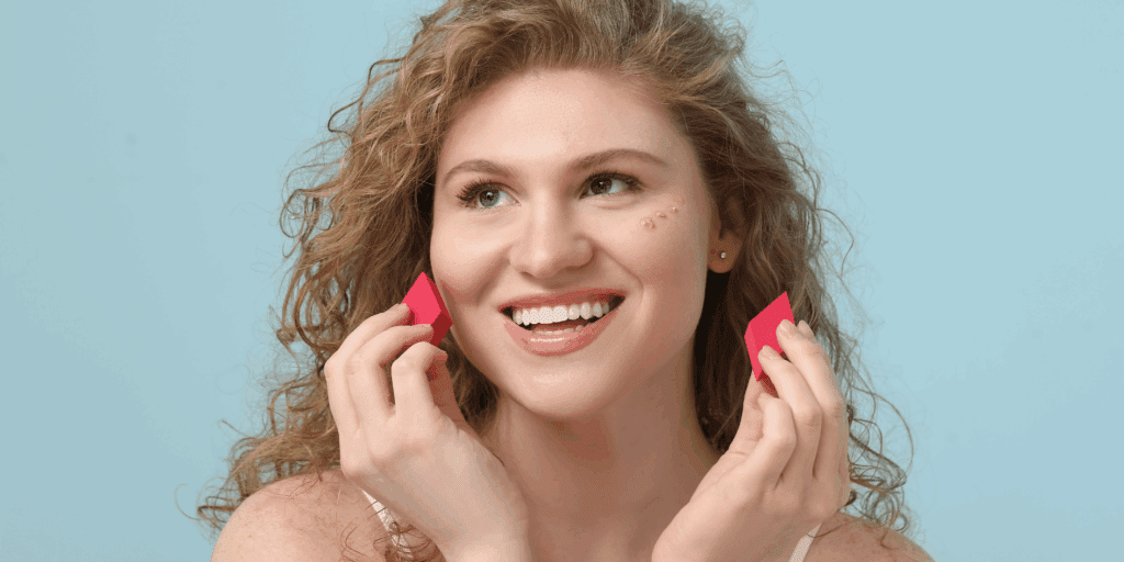  Close-up de uma mulher aplicando base com uma esponjinha úmida para um acabamento natural.