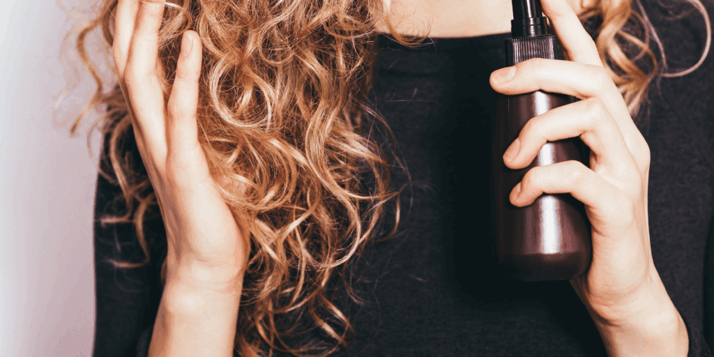 Mão aplicando um óleo reparador leve nas pontas de um cabelo saudável.