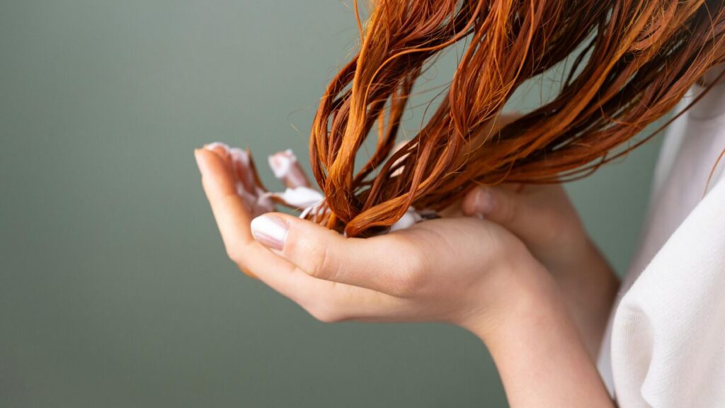 Mulher ruiva com cabelos molhados passando creme nos cabelos