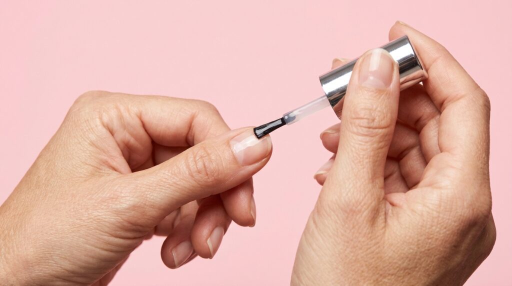 Mulher aplicando base fortalecedora transparente em suas unhas naturais curtas e elegantes.